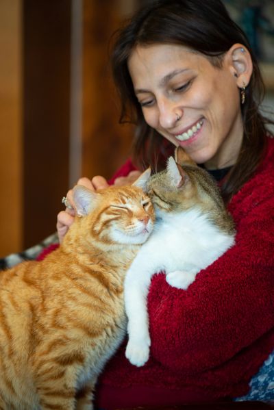Woman happily cuddling two affectionate cats.