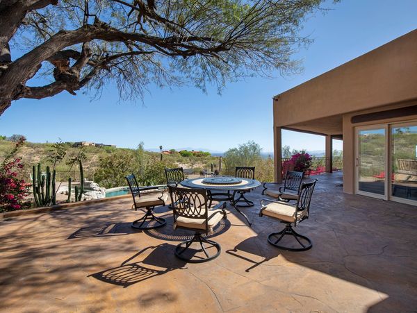 Outdoor patio with round table and chairs under a tree on a sunny day.