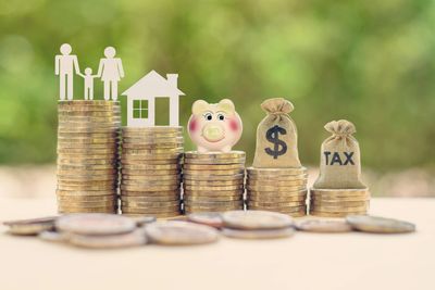 Stacks of coins with family, house, piggy bank, and tax symbols representing financial planning.