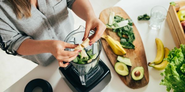 Person putting vegetables in a blender.