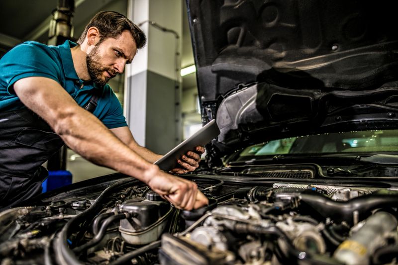 Mechanic using digital tablet in auto repair shop. He is analyzing engine stats.
