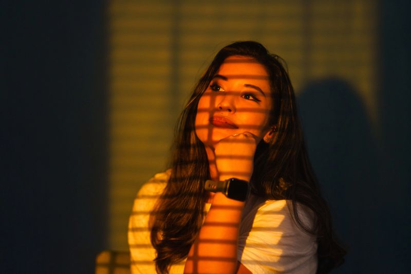 A portrait of a beautiful woman with warm light lighting her face and blinds of windows making shadows.