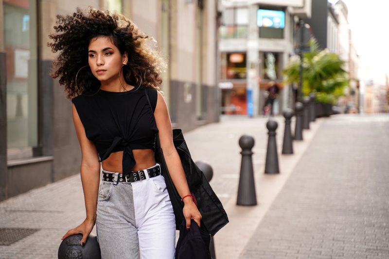 Photo of young fashionable colombian woman with afro hairstyle walking on the city street.