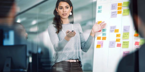 Woman presenting ideas using colorful sticky notes on a whiteboard in a meeting.