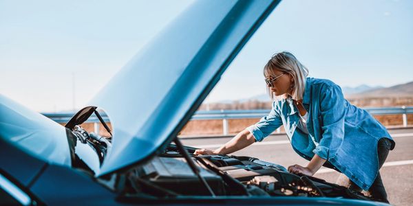 Woman checking car engine on roadside with hood open.