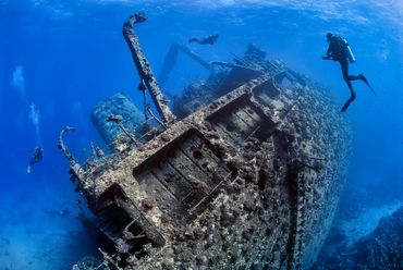 Divers exploring a large sunken shipwreck underwater.