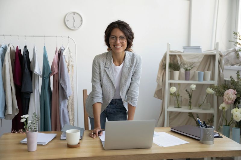 When hobby becomes business. Portrait of successful young woman designer dressmaker florist looking at camera with happy smile. Female owner of workshop studio atelier posing by desk enjoying work