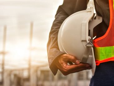 Person hält einen Sicherheitshelm auf einer Baustelle.
