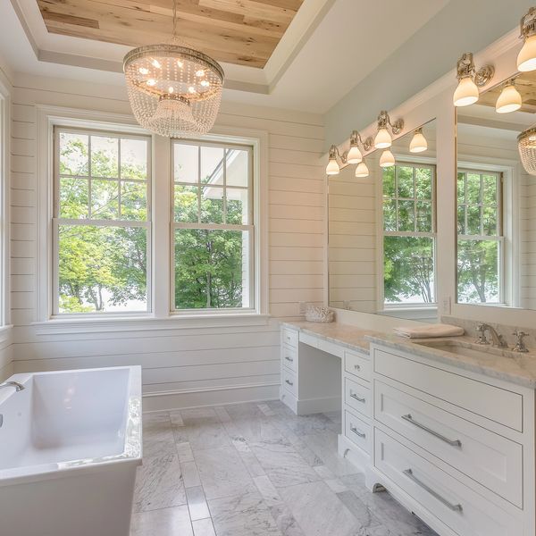 Bright, modern bathroom with large windows and elegant chandelier.