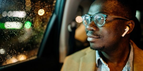 Man wearing glasses and earbuds looking out rainy car window at night.