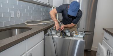 Technician repairing a dishwasher in a modern kitchen.