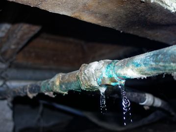 Leaking old metal pipe dripping water in a dark confined space.