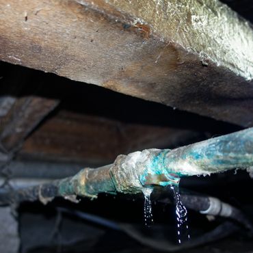 Old rusty pipe leaking water in a dark basement.
