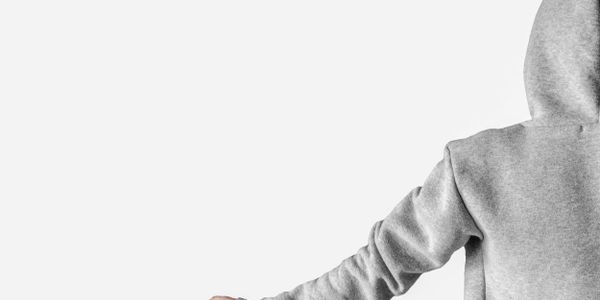 Person in gray hoodie reaching out with hand against a plain white background.
