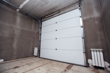 Empty garage with a closed white sectional door and concrete walls.
