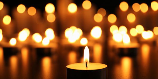 A single lit candle in focus with blurred candles glowing warmly in the background.