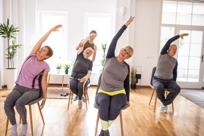 Seniors doing seated side stretches in a bright, spacious room.