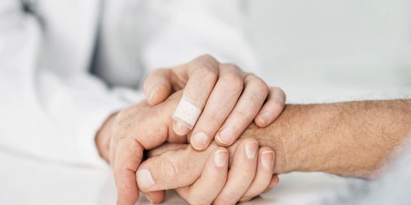 A doctor gently holding a patient's hand in a comforting gesture.