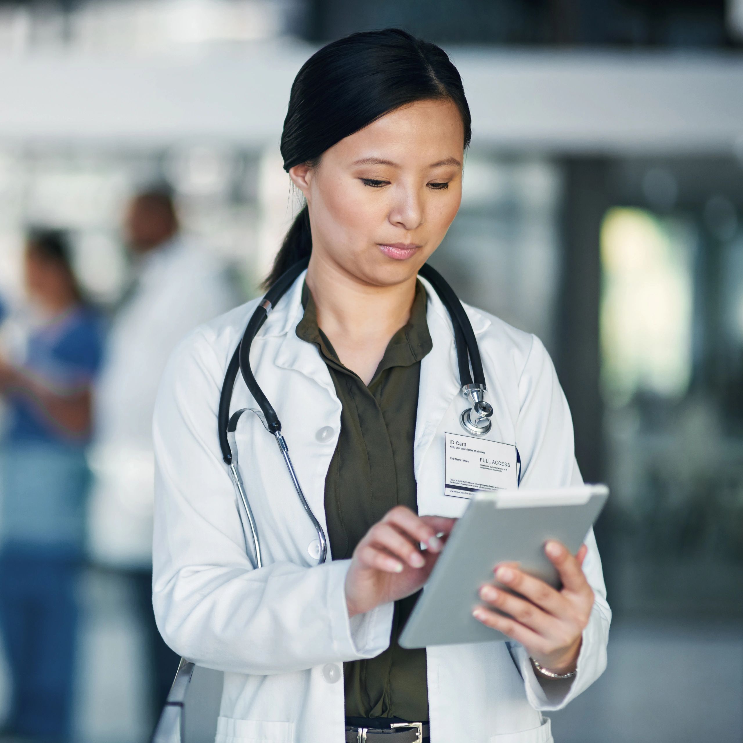 A female doctor in a white coat using a tablet in a hospital.