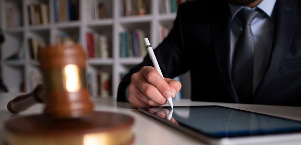 Person signing a digital contract on a tablet with a laptop nearby.
