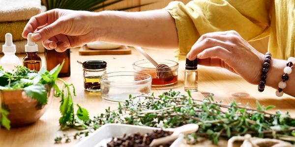 Hands preparing natural herbal remedies with essential oils and fresh herbs.