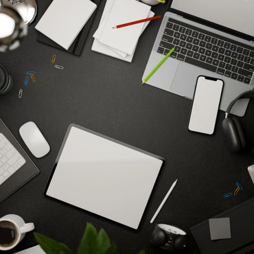 A modern workspace with a tablet, laptop, smartphone, and office supplies on a dark desk.