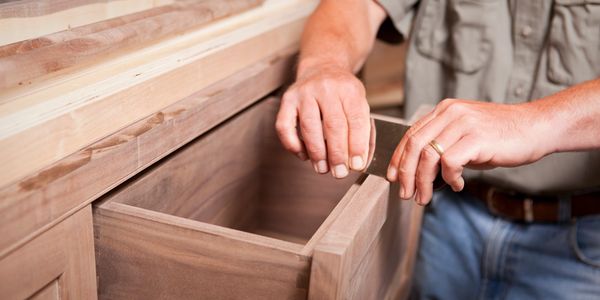 A craftsman sanding a wooden drawer in a workshop.
