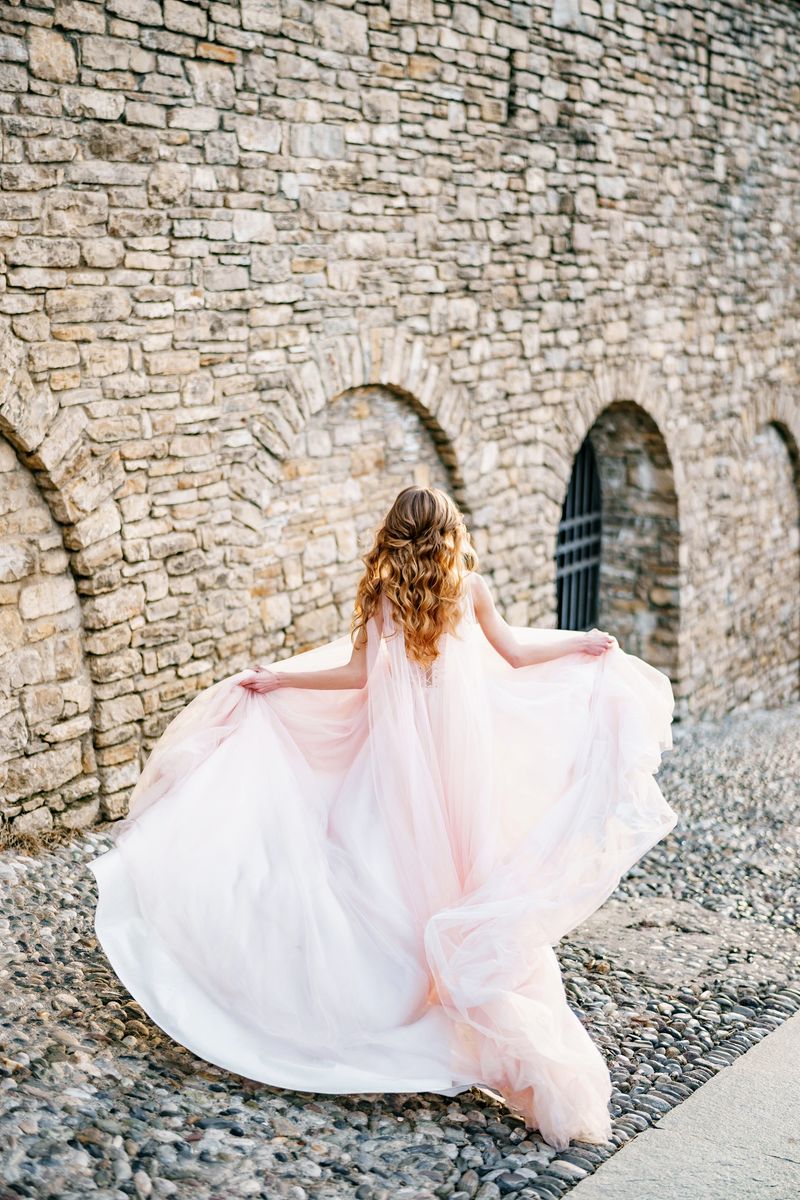Bride in a fluttering pink dress in the wind runs along the old street in Bergamo, Italy. Back view. High quality photo