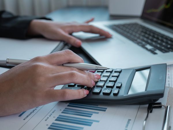 Person using a calculator and laptop for financial analysis with charts.