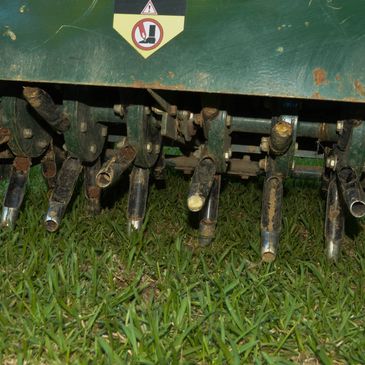 Close-up of a rusty agricultural machine part with blades on grass.
