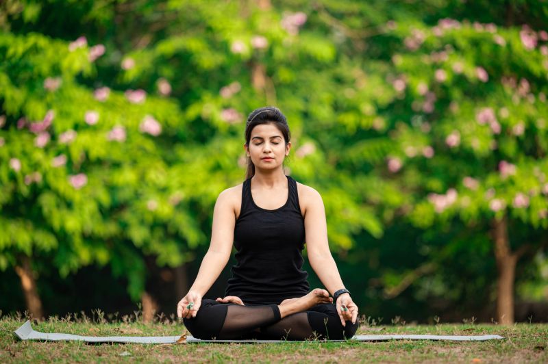 Young Asian/ Indian woman wearing black sports dress and meditating outdoors at park.