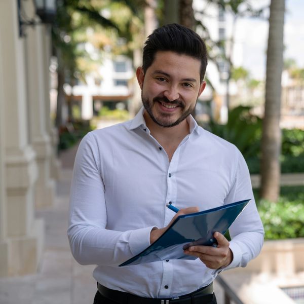 Smiling man in white shirt holding a clipboard outdoors.