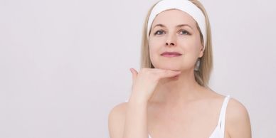 Middle-aged woman in white headband touching her chin, looking confident.