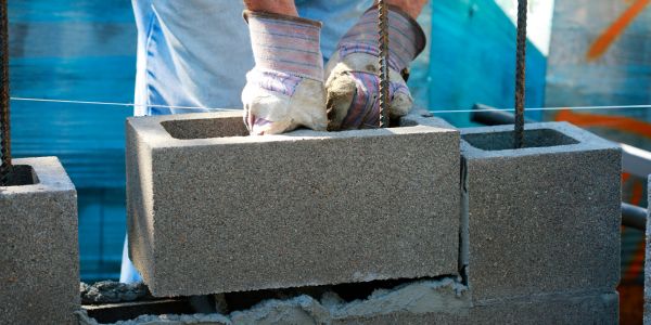 Worker laying concrete blocks wearing gloves.