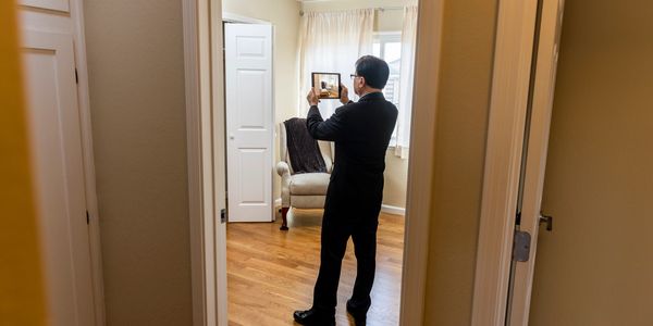 Man in suit takes a photo of a chair in a room with an iPad.