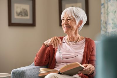 Caucasian senior lady with short grey hair and red shirt, smiling and holding her spectacles