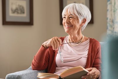 Elderly woman smiling while reading a book.
