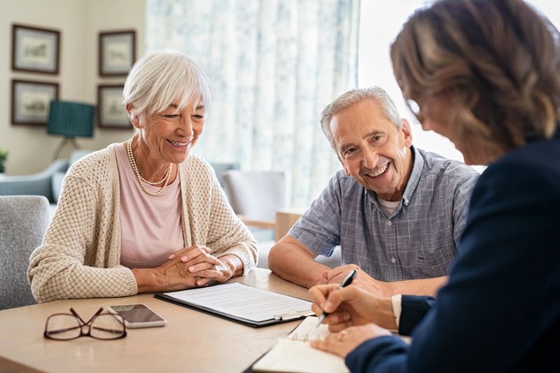 Senior couple planning their investments with financial advisor at home. Happy aged couple planning their medical insurance with advisor in living room. Old couple consulting with insurance agent while sitting together at home.