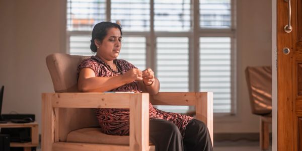 Woman sitting in a wooden chair, focused on her hands.