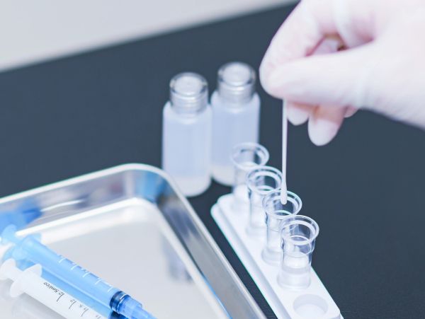 Gloved hand using a swab with lab vials and syringe.