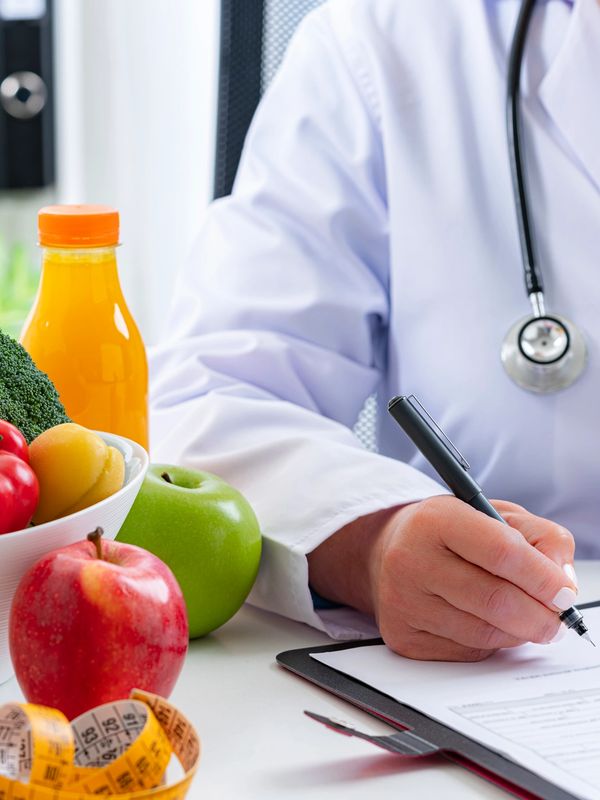 Doctor writing with fresh fruits and measuring tape on table.