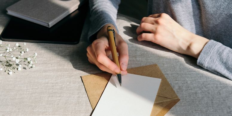 Person writing on a blank card with a pen on a table