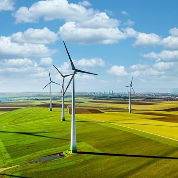Wind turbines on green and yellow farmland under a blue sky with clouds.