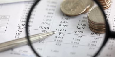 Magnifying glass, coins, and pen on a financial spreadsheet.