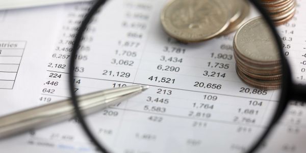 Magnifying glass, pen, and coins on financial document.