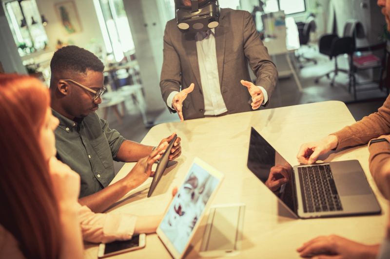 Depicting a team of VR specialists testing a new video game. One of them is telling them what he sees while the others are taking notes.