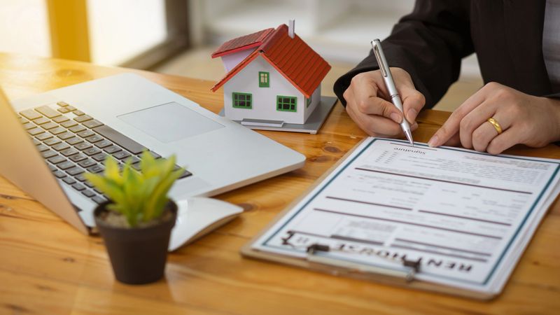 Real estate agents advise clients to rent or buy houses with contract documentation and laptop on their desk.