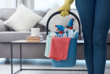 Person holding a bucket of cleaning supplies indoors.