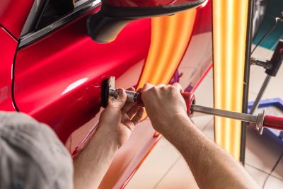 Person fixing a dent on a red car.