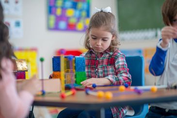 Young girl focused on building with colorful blocks in classroom.